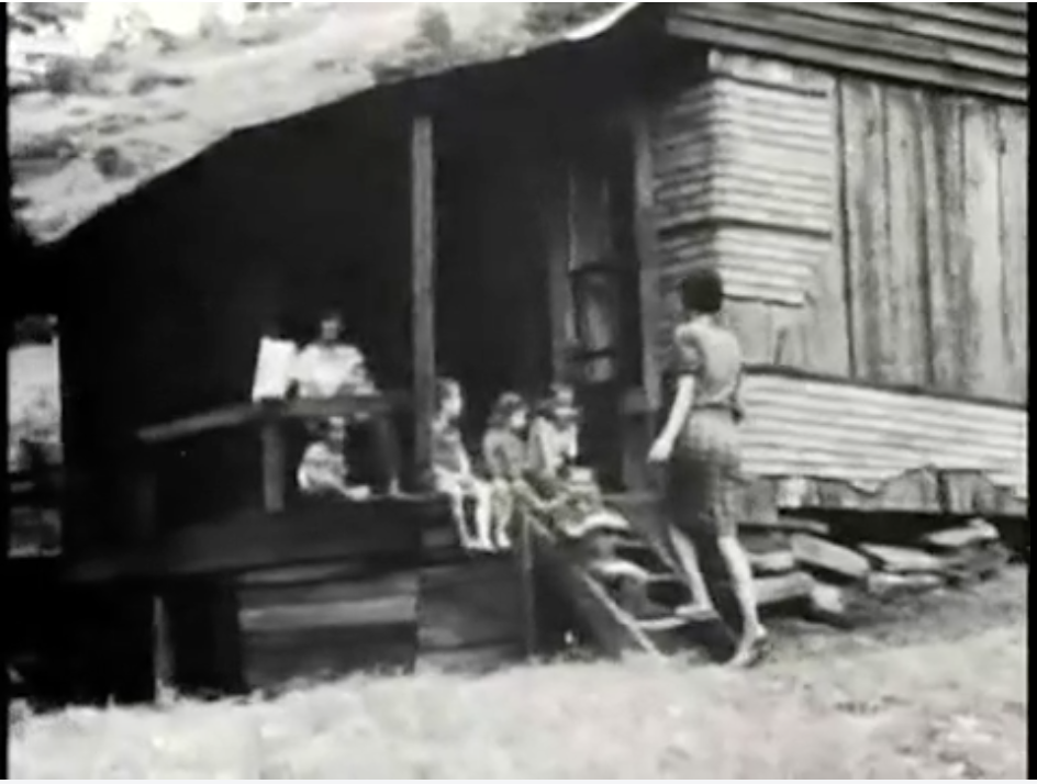 A still image of a poor family outside a shack in the film Stranger with a Camera