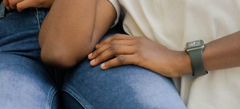 person in white shirt rests their hand on a person's leg in blue denim jeans